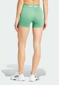 Gröna sportshorts med en figursydd design, hög midja med vita logodetaljer, kombinerade med vita sportskor.