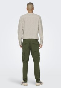 Hellbeige Langarmhemd, khakifarbene Cargo-Hose mit Seitentaschen und weiße Sneakers mit dunklen Akzenten, von hinten gesehen.