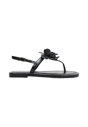 Sandalia plana negra con correa en el tobillo y detalle decorativo de flor en la parte superior estilo tanga, vista de lado sobre fondo blanco.