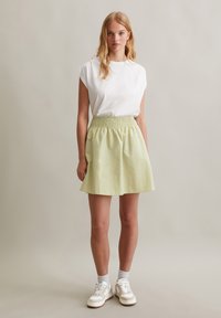 Witte katoenen t-shirt met korte, opgerolde mouwen, gecombineerd met een lichtgroene, uitlopende rok met een smock tailleband, en witte sneakers.
