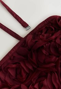 Burgundi viršus su audinio gėlių aplikacijomis. Turi plonas petnešas ir sidabrinę užsegimą, tekstūruotas gėlių dizainas visame paviršiuje.