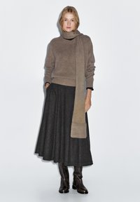 Brauner Strickpullover mit hohem Kragen, grauer gemusterter Rock und kniehohe braune Lederstiefel, kombiniert mit einem passenden Schal.