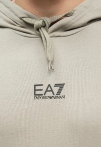 Φόρμα σε ανοιχτό μπεζ χρώμα με κορδόνι δέσιμο και το λογότυπο EA7 Emporio Armani τυπωμένο μαύρο στο στήθος.