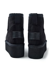 Botines negros de ante con suela de plataforma, paneles laterales elásticos y un dorso texturizado con detalles de marca. Acabado suave y diseño resistente.