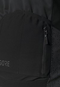 Kurtka GORE z czarnym materiałem, zamykana na zamek błyskawiczny kieszeń, gładką fakturą oraz boczną panelą w kropkowany wzór.