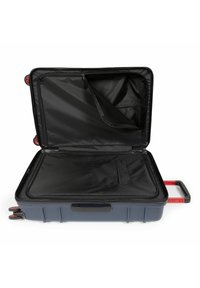 Hard-sided suitcase in dark grey with red accents. Interior features black fabric, multiple compartments, and a retractable handle.