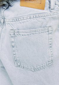 Jeans de mezclilla azul claro con un bolsillo trasero rectangular que presenta sutiles detalles de costura y una etiqueta de cuero marrón etiquetada "JONES."