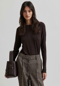 Barna, hosszú ujjú felső texturált, szürke nadrággal párosítva, amelyen foltos minták találhatók. A modell egy kicsi, sötétbarna táskát tart, amelynek elegáns fogantyúja van.