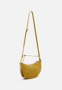Geel suède crossbodytas met een gebogen vorm, verstelbare schouderriem en gouden hardwareaccenten. Soepele textuur met een ritssluiting.