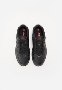 Czarne sneakersy z gładkiej skóry, okrągłym czubkiem, sześcioma otworami na sznurowadła i czarnymi sznurówkami. Na wkładkach widnieje czerwone logo "HUGO".