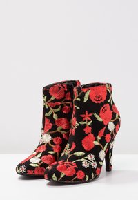 Schwarze Stiefeletten mit hohen Absätzen, die mit einem floral gestickten Muster in Rot, Grün und Weiß verziert sind. Glatte Textur und spitzes Design.