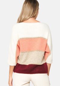 Neulepaita leveällä pääntiellä, jossa vaakasuorat raidat väriltään kerma, persikka, beige ja viininpunainen. Löysä istuvuus ja lasketut hartiasaumat.