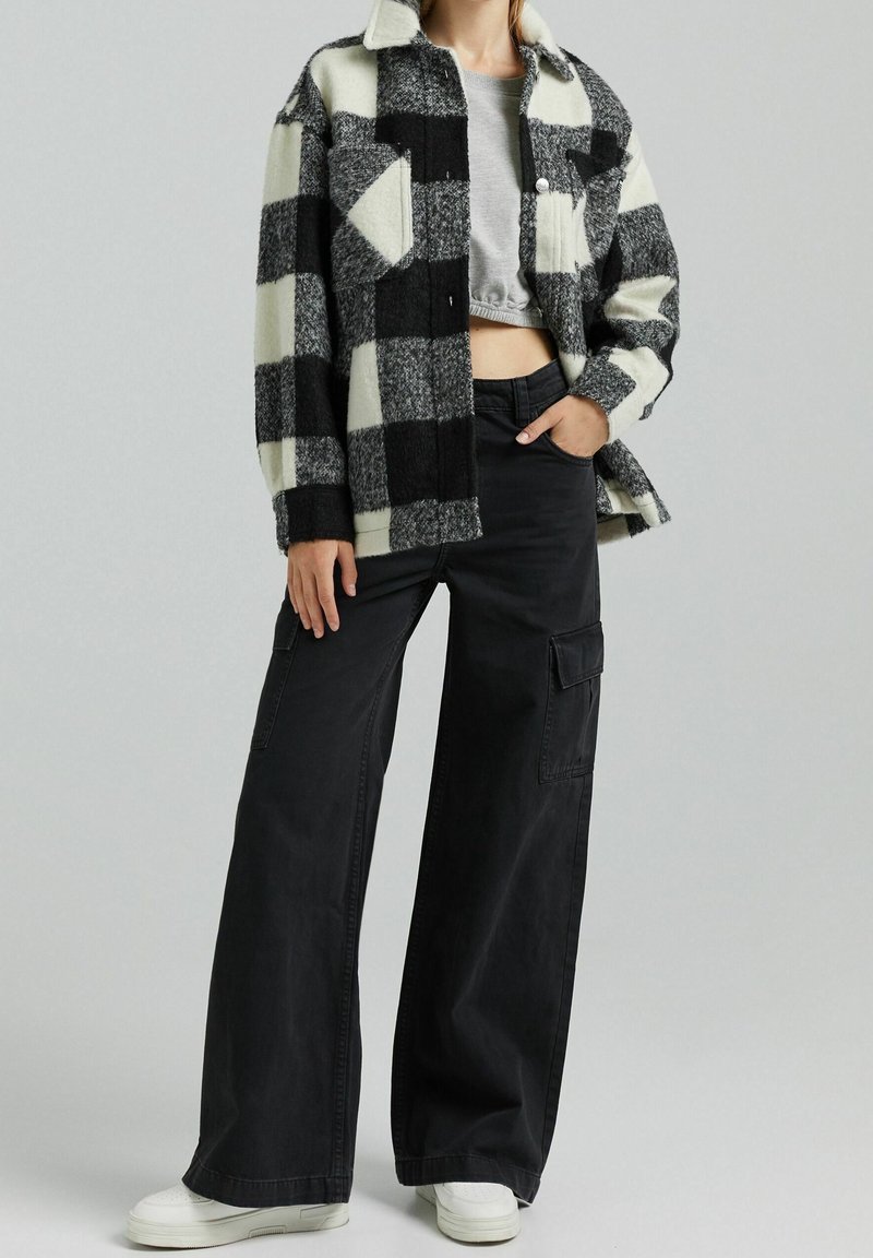 Svart och vit rutigt ulljacka med krage, knäppning och fickor. I kombination med högmidjade vida svarta byxor.