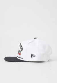 Bela kapa z belim šiltom, ki vključuje vezenine in napis, povezan z Atlanta Braves. Na strani je logotip.