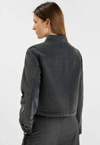 Chaqueta de mezclilla negra recortada con cuello clásico, mangas largas y detalles de costura visibles. La tela parece ligeramente texturizada.