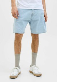 Shorts de mezclilla de un azul claro con un corte relajado, dobladillo deshilachado y diseño clásico de cinco bolsillos, combinados con zapatillas blancas y calcetines grises.
