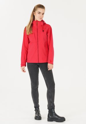 Red waterproof jacket with a zip front, adjustable hood, and side pockets, paired with black skinny jeans and black ankle boots.
