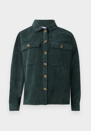 Camisa de pana en verde oscuro. Presenta un cuello con solapa, cierre frontal de botones y dos bolsillos en el pecho. Textura acanalada vertical.