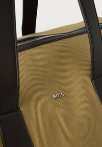 Τσάντα από ταμπά ύφασμα με μαύρα δερμάτινα λουριά και φερμουάρ, με μικρό ασημί λογότυπο «BOSS» στην μπροστινή πλευρά.
