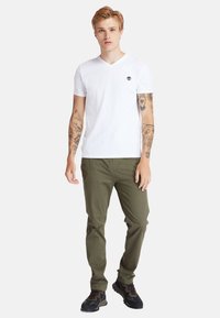 Vit bomull v-ringad t-shirt med en liten logotyp på bröstet, tillsammans med olivgröna byxor och svarta texturerade sneakers.