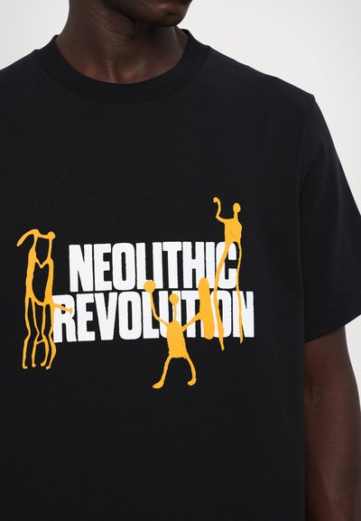 Sort bomulds t-shirt med iøjnefaldende gule grafikker af abstrakte figurer og teksten "NEOLITHIC REVOLUTION", der fremhæver et grafisk design.