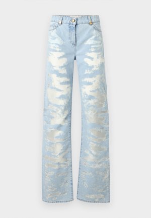 Blugi largi de culoare bleu deschis, cu pete albe uzate și închidere cu nasture auriu, pe un fundal simplu.