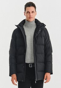 Czarna kurtka puchowa z zamkiem z przodu, dużym kołnierzem i pikowanym wzorem. Nosić na szary sweter z golfem i czarne spodnie. Matowa tekstura.