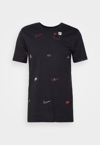 Camiseta negra de algodón con logotipos de Nike en blanco y rojo dispersos. Cuello redondo y mangas cortas, con diferentes colocaciones de logotipos.