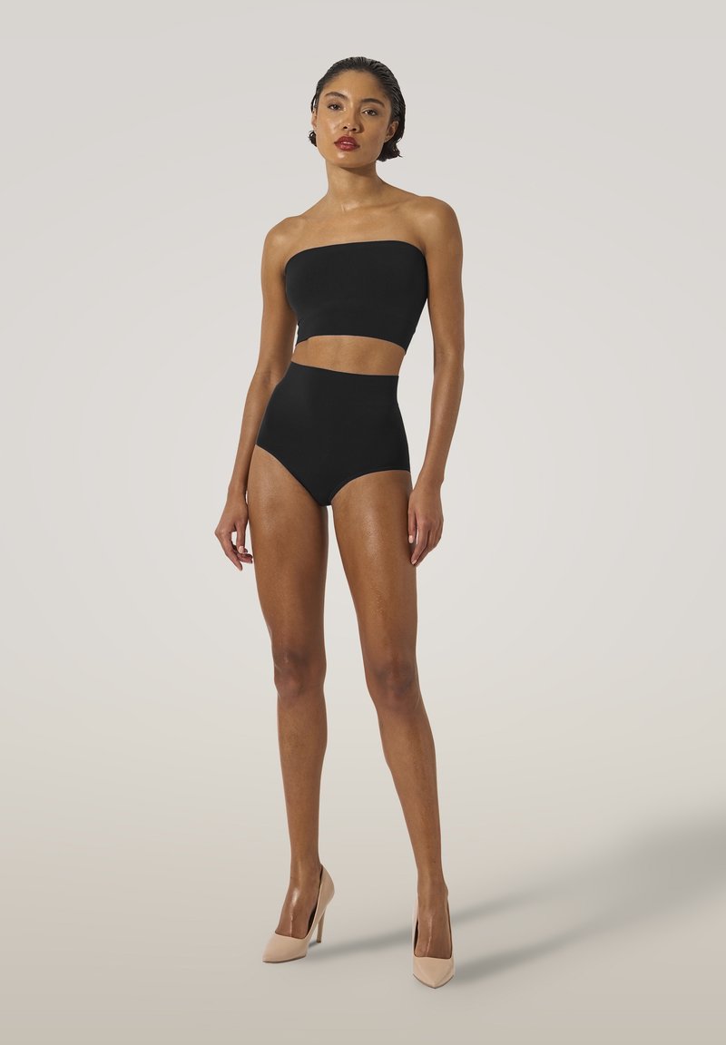 Svart strapless cropped topp i kombination med högmidjade bikiniunderdelar, med en slät textur och minimalistisk design. Bärs med nude högklackade skor.