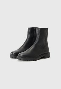 Botas de cuero negras hasta el tobillo con una superficie texturizada, cremallera lateral y suela de goma estriada para tracción. Corte recto y minimalismo en los detalles.