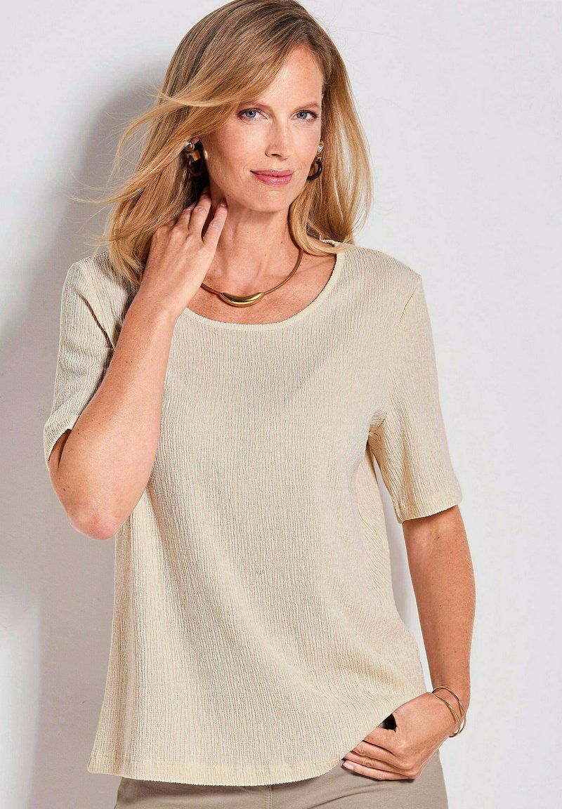 Beige top met korte mouwen, voorzien van een subtiele verticale textuur en een ronde hals. Beschikt over een lichte A-lijn vorm en zachte, ademende stof.