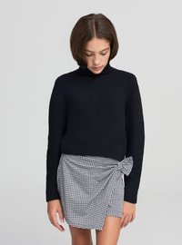 Dolcevita nero aderente in tessuto morbido abbinato a una minigonna pied de poule bianca e nera con dettaglio a fiocco.