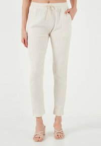 Licht beige, elastische taille broek met een trekkoord, voorzien van verticale witte strepen en een taps ontwerp. Zachte textuur met een casual pasvorm.