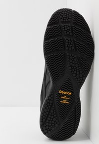 Suela de zapato Reebok negra que presenta material de goma, patrón de banda de rodadura texturizado y marcas naranjas resistentes al aceite y al deslizamiento.