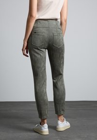 Grå mockaliknande byxor med slim fit, smala ben och två bakfickor, som bärs med vita sneakers. Slät textur och ren design.