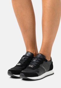 Czarne buty sportowe z połączeniem fakturowanej czarnej zamszowej skóry i gładkiej skóry, z subtelnym wzorem logo oraz białą podeszwą. Sznurowany design.