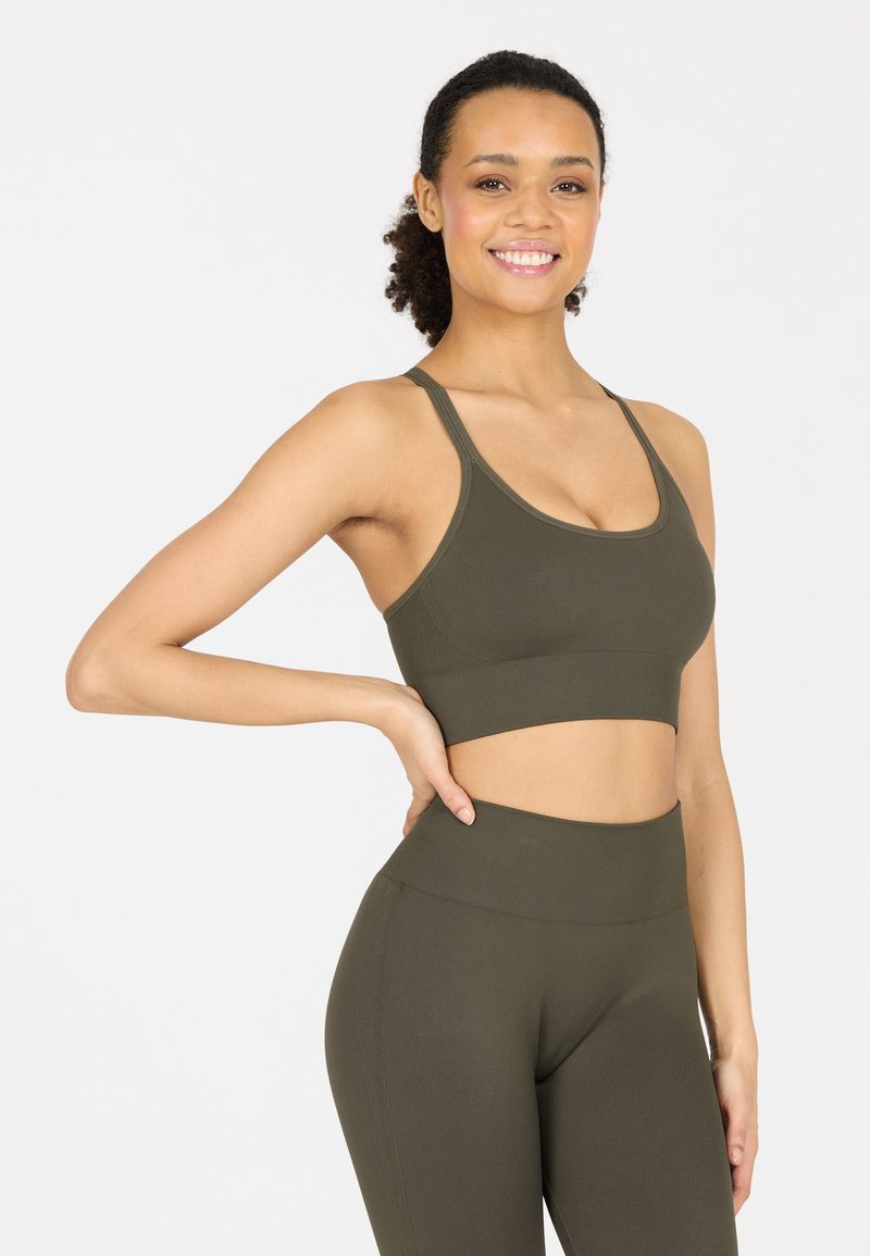 Olivgrüner Sport-BH mit einem figurnahen Design, dünnen Trägern und glatter Textur, kombiniert mit passenden hochgenähten Leggings.