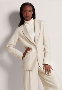 Crème-kleurige op maat gemaakte blazer met een reverskraag, twee knopen en subtiele verticale strepen, gecombineerd met wijde broekspijpen.