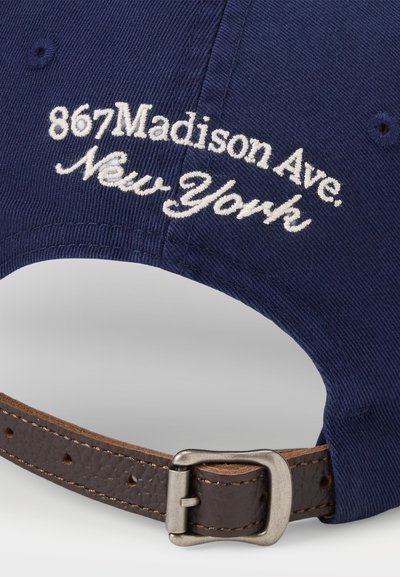 Sötétkék baseball sapka fehér hímzett "867 Madison Ave. New York." felirattal. Barna bőrszíjjal és fémből készült csattal rendelkezik.