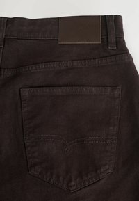 I jeans in denim marrone presentano una tasca posteriore con un motivo di cucitura curvato e una etichetta del marchio in pelle marrone sul passante della vita.