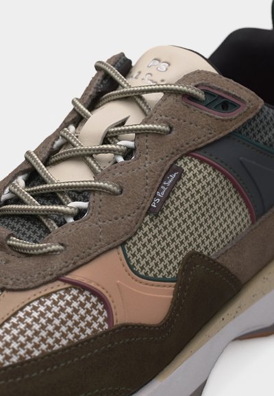 Κοντινή λήψη καφέ αθλητικού παπουτσιού με ύφασμα καρό κυνός, μπεζ και ροζ λεπτομέρειες, μπεζ κορδόνια και ετικέτα "PS Paul Smith" στο πλάι.