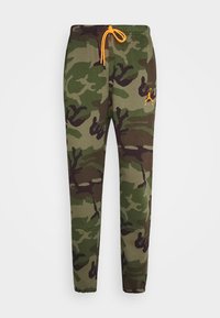 Kamouflage joggerbyxor i nyanser av grön och brun, med ett elastiskt midjeband och en orange dragkedja samt en liten logotyp på låret.