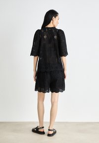 Robe noire en dentelle avec des découpes florales, dotée de manches courtes, d'un ourlet festonné, et assortie de sandales noires.