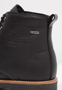 Botas de cuero negro hasta el tobillo con una superficie texturada, que presentan una etiqueta Gore-Tex, detalles de costura y una suela de goma marrón.