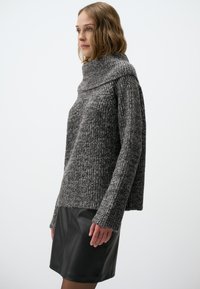 Pull en tricot gris avec un large col roulé, des manches longues et une texture agréable, associé à une jupe en cuir noir.