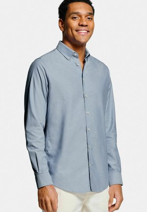 Chemise bleu clair à manches longues avec col et poignets boutonnés, en tissu lisse avec un ourlet droit et des boutons.