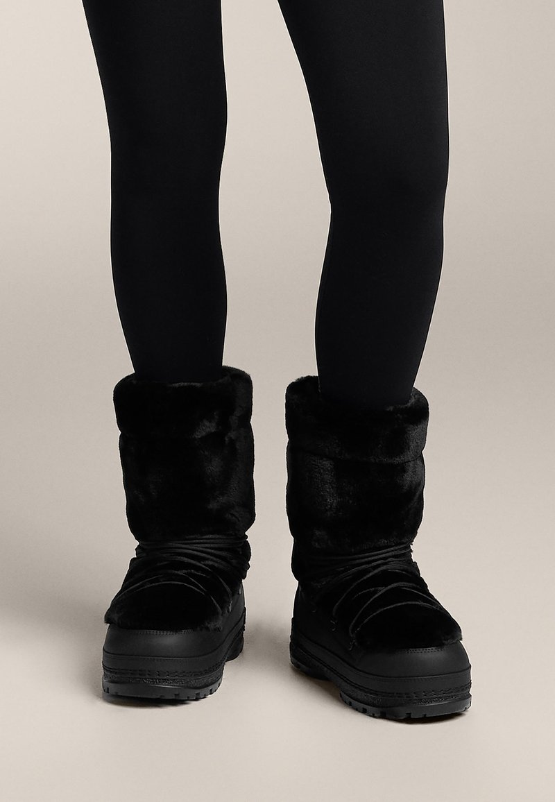 Sorte vinterstøvler med en manchet af imiteret pels, tekstureret fløjlmateriale, rund tå og en robust gummisål for godt greb.