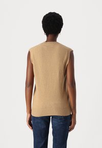 Ärmelloser beiger Pullover mit geripptem Rundhalsausschnitt, der eine weiche Textur und einen geraden Schnitt aufweist. Die Rückansicht zeigt glatte Nähte und Kanten.