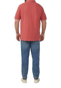 Czerwona bawełniana koszulka polo, krótki rękaw, prosty krój, w połączeniu z jasnoniebieskimi dżinsami, casualowy krój, oraz białe trampki z ciemnymi akcentami na pięcie.