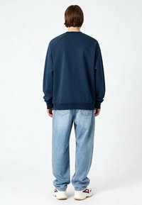 Sweat-shirt bleu marine à manches raglan, col rond et poignets côtelés, associé à un jean en denim bleu clair à coupe ample et des baskets blanches.